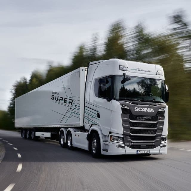A white Scania refrigerated truck travelling at speed on the motorway.